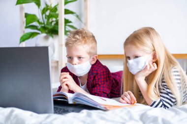Uzaktan öğrenme çevrimiçi eğitim. Hasta okul çocuğu ve maskeli kız evde dijital tablet dizüstü bilgisayarla ders çalışıyor ve ödev yapıyor. Eğitim kitaplarıyla yatakta oturmak.