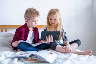 Uzaktan öğrenme çevrimiçi eğitim. Öğrenci çocuk ve kız evde dijital tablet dizüstü bilgisayarla ders çalışıyor ve okul ödevi yapıyor. Eğitim kitaplarıyla yatakta oturmak..