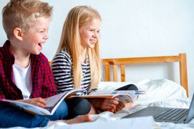 Uzaktan öğrenme çevrimiçi eğitim. Öğrenci çocuk ve kız evde dijital tablet dizüstü bilgisayarla ders çalışıyor ve okul ödevi yapıyor. Eğitim kitaplarıyla yatakta oturmak..