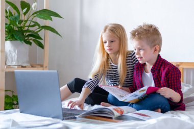 Uzaktan öğrenme çevrimiçi eğitim. Öğrenci çocuk ve kız evde dijital tablet dizüstü bilgisayarla ders çalışıyor ve okul ödevi yapıyor. Eğitim kitaplarıyla yatakta oturmak..