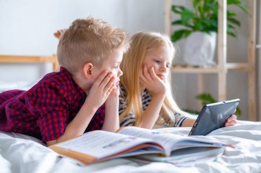 Uzaktan öğrenme çevrimiçi eğitim. Öğrenci çocuk ve kız evde dijital tablet dizüstü bilgisayarla ders çalışıyor ve okul ödevi yapıyor. Eğitim kitaplarıyla yatakta oturmak..