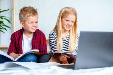 Uzaktan öğrenme çevrimiçi eğitim. Öğrenci çocuk ve kız evde dijital tablet dizüstü bilgisayarla ders çalışıyor ve okul ödevi yapıyor. Eğitim kitaplarıyla yatakta oturmak..