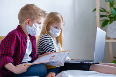 Uzaktan öğrenme çevrimiçi eğitim. Hasta okul çocuğu ve maskeli kız evde dijital tablet dizüstü bilgisayarla ders çalışıyor ve ödev yapıyor. Eğitim kitaplarıyla yatakta oturmak.