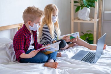 Uzaktan öğrenme çevrimiçi eğitim. Hasta okul çocuğu ve maskeli kız evde dijital tablet dizüstü bilgisayarla ders çalışıyor ve ödev yapıyor. Eğitim kitaplarıyla yatakta oturmak.