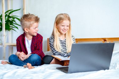 Uzaktan öğrenme çevrimiçi eğitim. Öğrenci çocuk ve kız evde dijital tablet dizüstü bilgisayarla ders çalışıyor ve okul ödevi yapıyor. Eğitim kitaplarıyla yatakta oturmak..