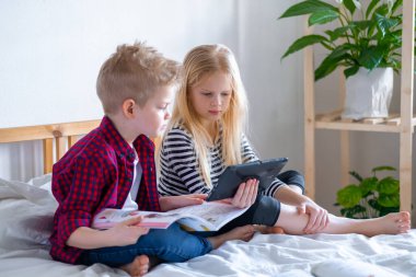 Uzaktan öğrenme çevrimiçi eğitim. Öğrenci çocuk ve kız evde dijital tablet dizüstü bilgisayarla ders çalışıyor ve okul ödevi yapıyor. Eğitim kitaplarıyla yatakta oturmak..