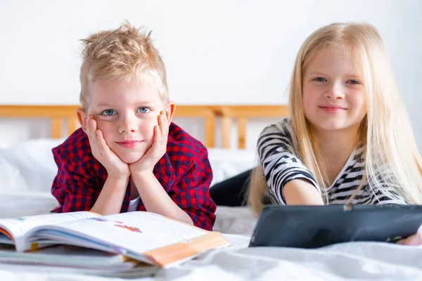 Enseignement à distance en ligne. Écolier et fille étudiant à la maison avec ordinateur portable tablette numérique ordinateur portable et faire des devoirs scolaires. Assis sur le lit avec des livres d'entraînement . — Photo