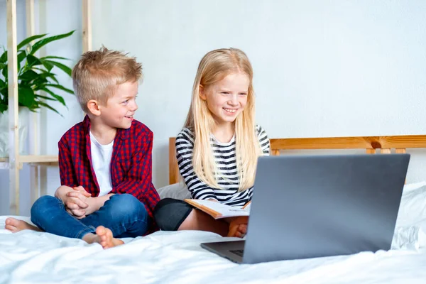Kształcenie online na odległość. Uczeń i dziewczyna uczą się w domu z notebooka tabletu cyfrowego i odrabiają lekcje w szkole. Siedzenie na łóżku z książkami treningowymi. — Zdjęcie stockowe