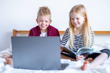 Uzaktan öğrenme çevrimiçi eğitim. Öğrenci çocuk ve kız evde dijital tablet dizüstü bilgisayarla ders çalışıyor ve okul ödevi yapıyor. Eğitim kitaplarıyla yatakta oturmak..