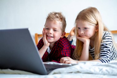 Uzaktan öğrenme çevrimiçi eğitim. Öğrenci çocuk ve kız evde dijital tablet dizüstü bilgisayarla ders çalışıyor ve okul ödevi yapıyor. Eğitim kitaplarıyla yatakta oturmak..
