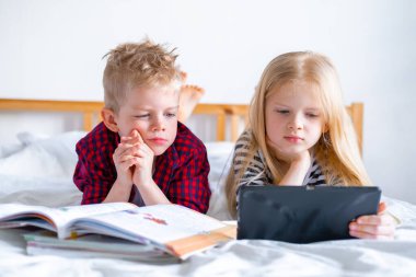 Uzaktan öğrenme çevrimiçi eğitim. Öğrenci çocuk ve kız evde dijital tablet dizüstü bilgisayarla ders çalışıyor ve okul ödevi yapıyor. Eğitim kitaplarıyla yatakta oturmak..