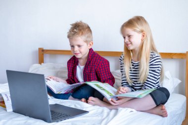 Uzaktan öğrenme çevrimiçi eğitim. Öğrenci çocuk ve kız evde dijital tablet dizüstü bilgisayarla ders çalışıyor ve okul ödevi yapıyor. Eğitim kitaplarıyla yatakta oturmak..