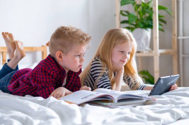 Uzaktan öğrenme çevrimiçi eğitim. Öğrenci çocuk ve kız evde dijital tablet dizüstü bilgisayarla ders çalışıyor ve okul ödevi yapıyor. Eğitim kitaplarıyla yatakta oturmak..