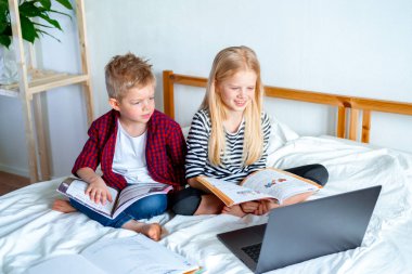 Uzaktan öğrenme çevrimiçi eğitim. Öğrenci çocuk ve kız evde dijital tablet dizüstü bilgisayarla ders çalışıyor ve okul ödevi yapıyor. Eğitim kitaplarıyla yatakta oturmak..