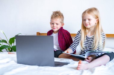 Uzaktan öğrenme çevrimiçi eğitim. Öğrenci çocuk ve kız evde dijital tablet dizüstü bilgisayarla ders çalışıyor ve okul ödevi yapıyor. Eğitim kitaplarıyla yatakta oturmak..