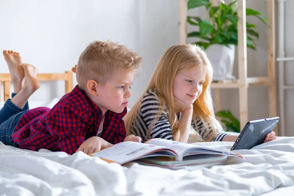 Kształcenie online na odległość. Uczeń i dziewczyna uczą się w domu z notebooka tabletu cyfrowego i odrabiają lekcje w szkole. Siedzenie na łóżku z książkami treningowymi. — Zdjęcie stockowe