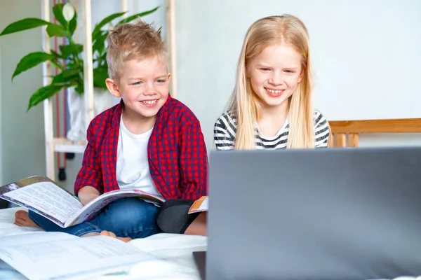 Kształcenie online na odległość. Uczeń i dziewczyna uczą się w domu z notebooka tabletu cyfrowego i odrabiają lekcje w szkole. Siedzenie na łóżku z książkami treningowymi. — Zdjęcie stockowe