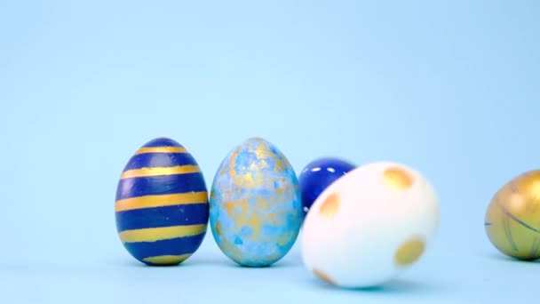 Los huevos de Pascua están rodando, golpeándose unos a otros en la mesa azul. Huevos de moda de color clásico azul, blanco y dorado. Feliz Pascua. Estilo mínimo. — Vídeos de Stock