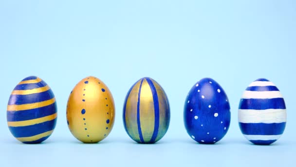 复活节彩蛋在滚动,互相敲打着蓝色的桌子.鸡蛋色彩艳丽,经典的蓝色、白色和金色.复活节快乐简约风格. — 图库视频影像