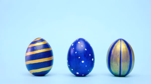 Los huevos de Pascua están rodando, golpeándose unos a otros en la mesa azul. Huevos de moda de color clásico azul, blanco y dorado. Feliz Pascua. Estilo mínimo. — Vídeos de Stock