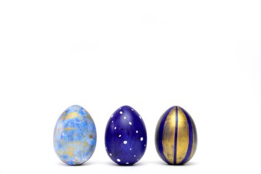 Üç Paskalya yumurtası, beyaz masanın üzerinde klasik mavi, beyaz ve altın renkli süslemeler. Mesaj için fotokopi alanı olan mutlu Paskalyalar. Asgari biçim