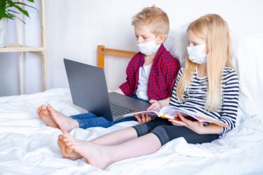 Uzaktan öğrenme çevrimiçi eğitim. Hasta okul çocuğu ve maskeli kız evde dijital tablet dizüstü bilgisayarla ders çalışıyor ve ödev yapıyor. Eğitim kitaplarıyla yatakta oturmak.