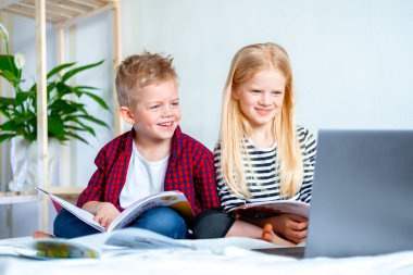 Uzaktan öğrenme çevrimiçi eğitim. Öğrenci çocuk ve kız evde dijital tablet dizüstü bilgisayarla ders çalışıyor ve okul ödevi yapıyor. Eğitim kitaplarıyla yatakta oturmak..