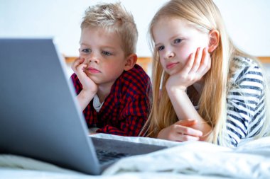 Uzaktan öğrenme çevrimiçi eğitim. Öğrenci çocuk ve kız evde dijital tablet dizüstü bilgisayarla ders çalışıyor ve okul ödevi yapıyor. Eğitim kitaplarıyla yatakta oturmak..