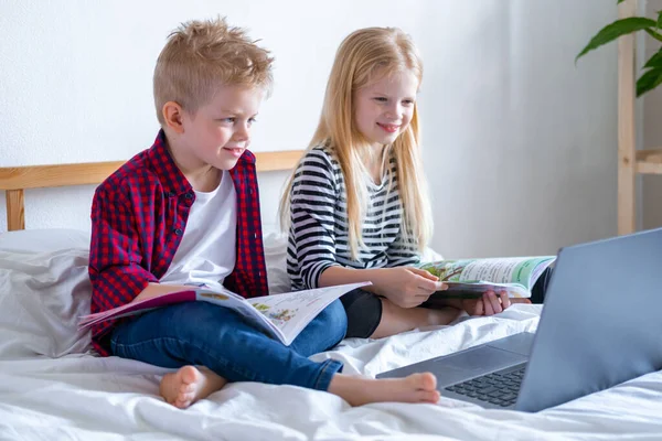 Uzaktan öğrenme çevrimiçi eğitim. Öğrenci çocuk ve kız evde dijital tablet dizüstü bilgisayarla ders çalışıyor ve okul ödevi yapıyor. Eğitim kitaplarıyla yatakta oturmak..