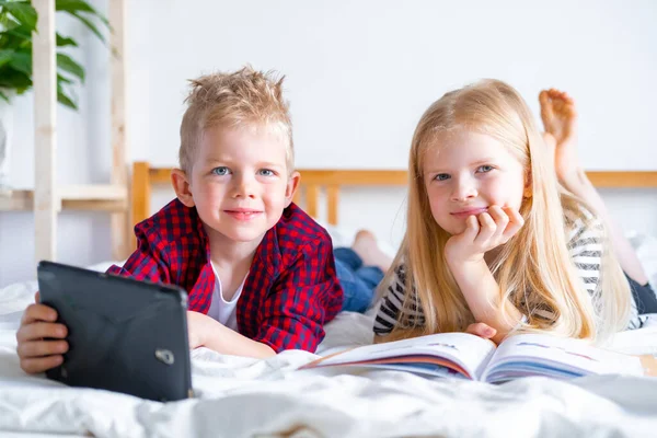 Uzaktan öğrenme çevrimiçi eğitim. Öğrenci çocuk ve kız evde dijital tablet dizüstü bilgisayarla ders çalışıyor ve okul ödevi yapıyor. Eğitim kitaplarıyla yatakta oturmak..