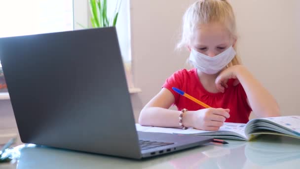 遠隔オンライン教育。自宅でデジタルタブレットを手に勉強し、学校の宿題をする医療マスクの病気の女子学生。テーブルの上で書籍やノートをトレーニング. — ストック動画