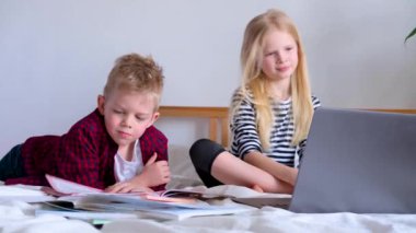 Uzaktan öğrenme çevrimiçi eğitim. Öğrenci çocuk ve kız evde dijital tablet dizüstü bilgisayarla ders çalışıyor ve okul ödevi yapıyor. Eğitim kitaplarıyla yatakta oturmak..