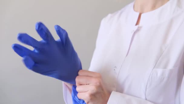 Una doctora cirujana en uniforme blanco se pone guantes azules. Concepto de higiene, tratamiento, medicina — Vídeos de Stock