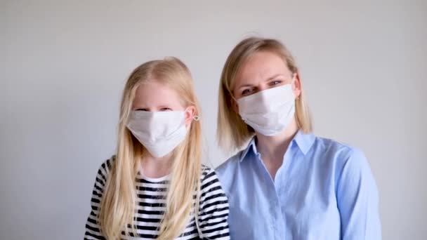 Glückliche blonde Mutter und Tochter mit chirurgischer medizinischer Gesichtsmaske gegen Infektionskrankheiten Schutz vor Erkältung gemeiner Grippe. Mädchen gucken in die Kamera, lachen, kuscheln — Stockvideo