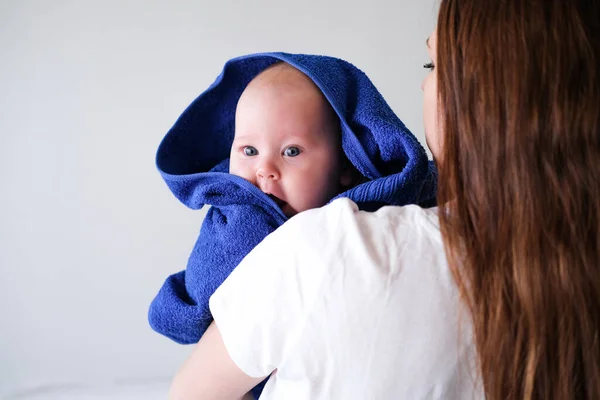 Mamãe abraça seu bebezinho mais fofo depois do banho com toalha azul na cabeça. Criança infantil em mãos de mãe. Amor maternal. Vida familiar. Mãe e bebé. Mãe feliz — Fotografia de Stock