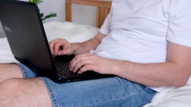 4K Tanınmayan Adam ofis çalışanı. Evden yatağın üzerinde çalışıyor. Bilgisayar kullanarak. Evde güvende kalma çağrısı. Uzaklık öğrenme çevrimiçi eğitim ve çalışma.