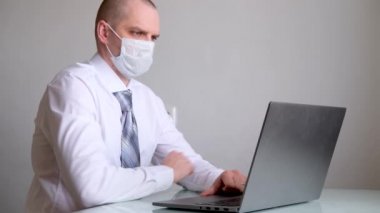 4K maskeli, ofis kıyafetli, beyaz gömlekli ve kravatlı bir adam ev bilgisayarından iş görüşmesi yapıyor. Evde güvende kalma çağrısı. Mesafe çalışması. Karantina