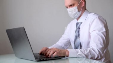 4K maskeli, ofis kıyafetli, beyaz gömlekli ve kravatlı bir adam ev bilgisayarından iş görüşmesi yapıyor. Evde güvende kalma çağrısı. Mesafe çalışması. Karantina