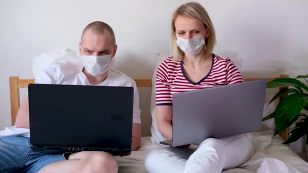 4k jonge familie werkt op afstand van huis op bed aan de computer. In quarantaine geplaatst koppel coronavirus met medische maskers. Blijf veilig thuis. Afstandsonderwijs, onderwijs en werk. Bestel levensmiddelen online — Stockvideo