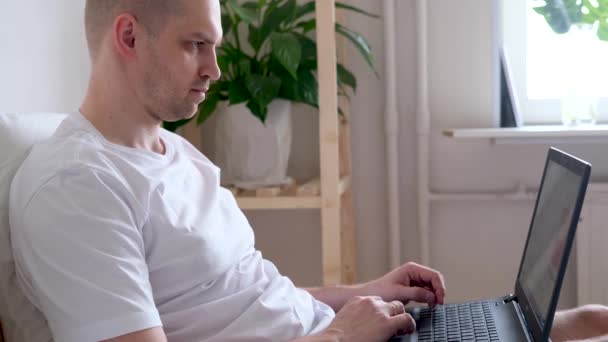 4k Man arbeitet im Büro von zu Hause aus im Bett. Mit dem Computer. Die Aufforderung, sicher zu Hause zu bleiben. Online-Fernstudium und Arbeit. — Stockvideo