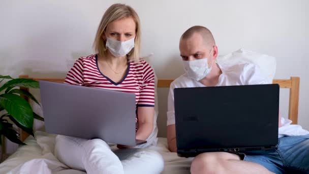 4k młoda rodzina pracuje zdalnie z domu na łóżku przy komputerze. Poddano kwarantannie kilka koronawirusów w maskach medycznych. Zostań w domu. Kształcenie na odległość, edukacja i praca. Zamów produkty spożywcze online — Wideo stockowe