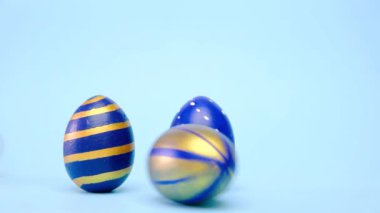 Paskalya yumurtaları yuvarlanıyor, birbirlerini mavi masaya vuruyorlar. Yumurtaların modası geçmiş klasik mavi, beyaz ve altın rengi. Mutlu Paskalyalar. Asgari biçim. 