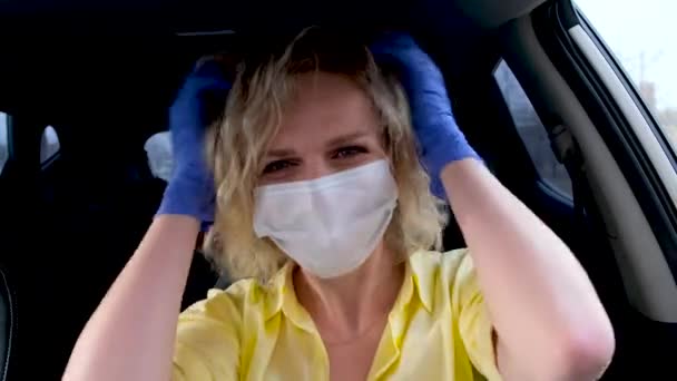 4k Curly szőke lány sofőr a nyári viselet és orvosi maszk és védőkesztyű egyenesíti a haját az autóban vezetés előtt. Nő a nátha ellen. Maradj otthon karanténban.. — Stock videók