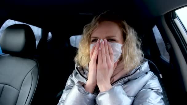 4k Lockige blonde Fahrerin setzt medizinische Maske und blaue Schutzhandschuhe im Auto vor der Fahrt auf. Frau in warmer Jacke gegen Erkältung. Bleiben Sie unter Quarantäne. — Stockvideo