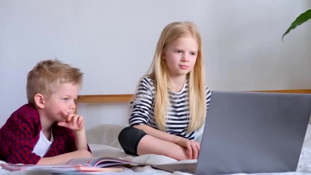 Online onderwijs op afstand. Schooljongen en meisje thuis studeren met digitale tablet laptop notebook en het doen van huiswerk op school. Op bed zitten met trainingsboeken. — Stockvideo