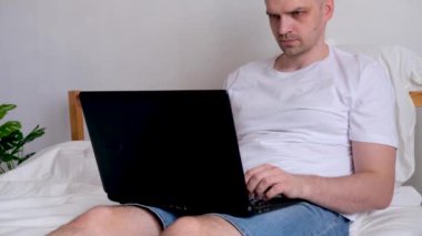 4K Man ofis işi evden yatağa kadar uzanıyor. Bilgisayar kullanarak. Evde güvende kalma çağrısı. Uzaklık öğrenme çevrimiçi eğitim ve çalışma.