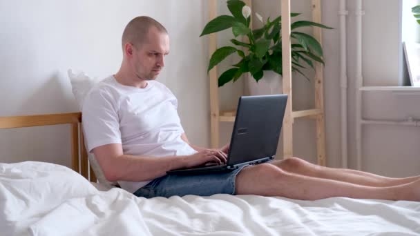 4k El hombre que trabaja la oficina trabaja remotamente de casa en la cama. Usando computadora. La llamada para estar a salvo en casa. Educación a distancia en línea y trabajo . — Vídeo de stock