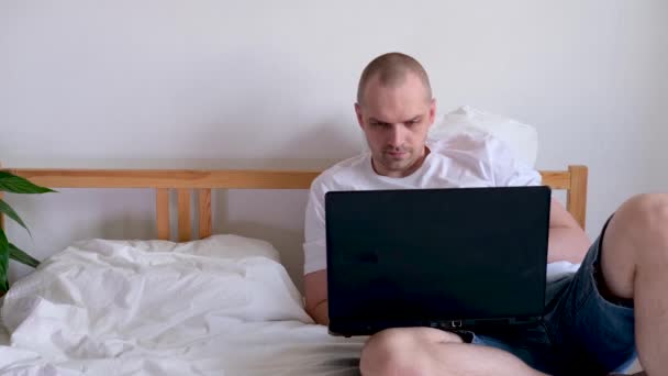 4k El hombre que trabaja la oficina trabaja remotamente de casa en la cama. Usando computadora. La llamada para estar a salvo en casa. Educación a distancia en línea y trabajo . — Vídeo de stock