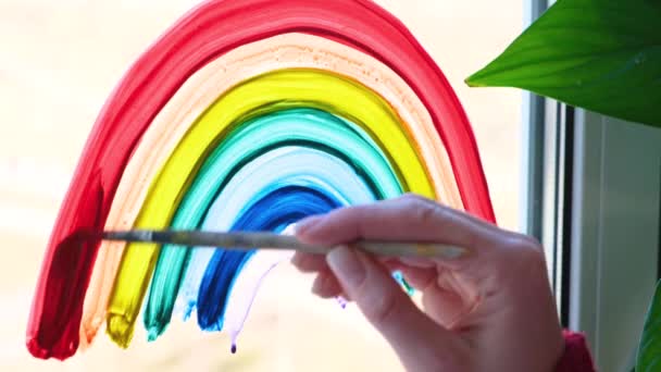 4k. Ragazza pittura arcobaleno sulla finestra durante Covid-19 quarantena a casa. Rimanere a casa campagna di social media per la prevenzione coronavirus, lascia che tutti siano bene, speranza. Cattura l'arcobaleno . — Video Stock