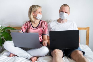 Genç aile evden uzakta bilgisayarın başında yatağında çalışıyor. Tıbbi maskeli karantina altındaki bir çift koronavirüs. Kendine dikkat et. Mesafe öğrenme, eğitim ve çalışma. İnternetten gıda siparişi